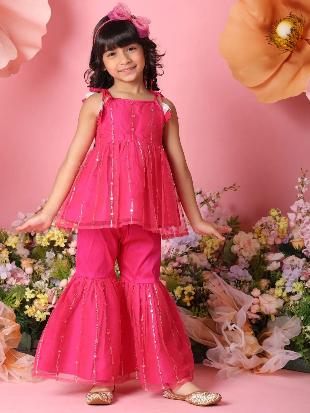 Young girl in a pink outfit standing among flowers on a pink background