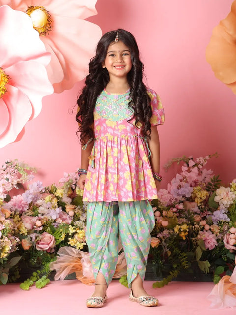 Young girl in a colorful traditional outfit standing against a pink floral background