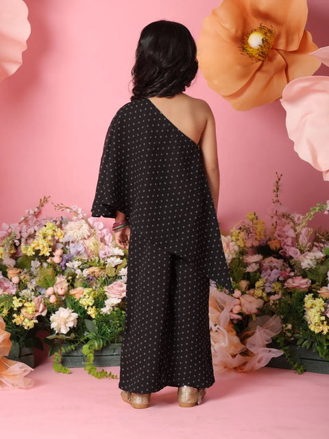 Person wearing a black polka dot dress standing in front of pink flowers and a pink background