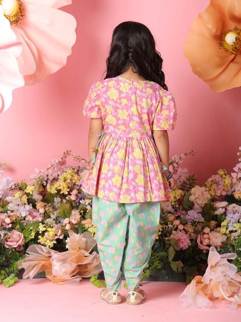 Child wearing a pink floral top and green pants with flowers and pink background