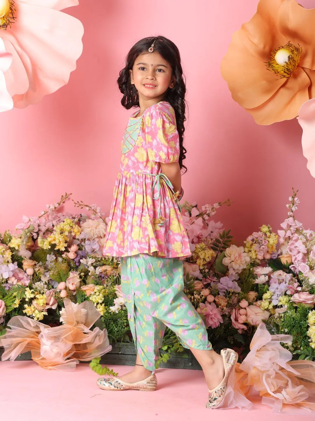 Young girl in a colorful outfit standing among flowers with a pink background