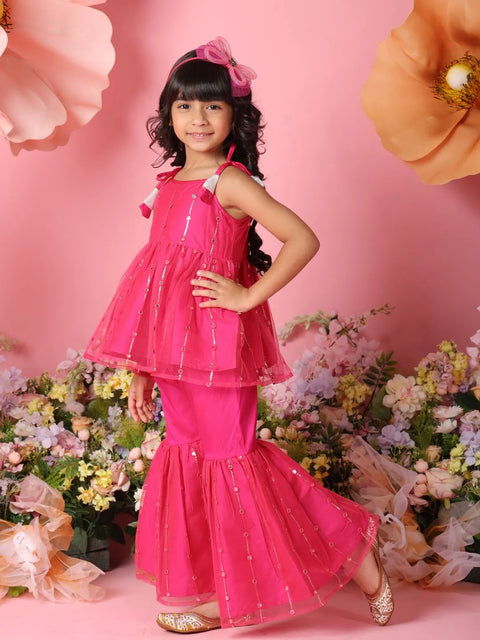Young girl in a pink traditional outfit standing against a pink background with flowers.