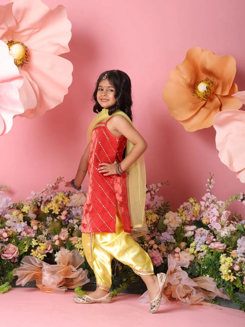 Young girl in a red and yellow traditional outfit standing against a pink floral backdrop