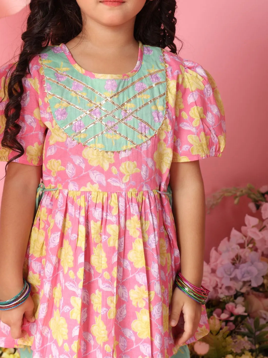 Child wearing a colorful dress with floral patterns against a pink background