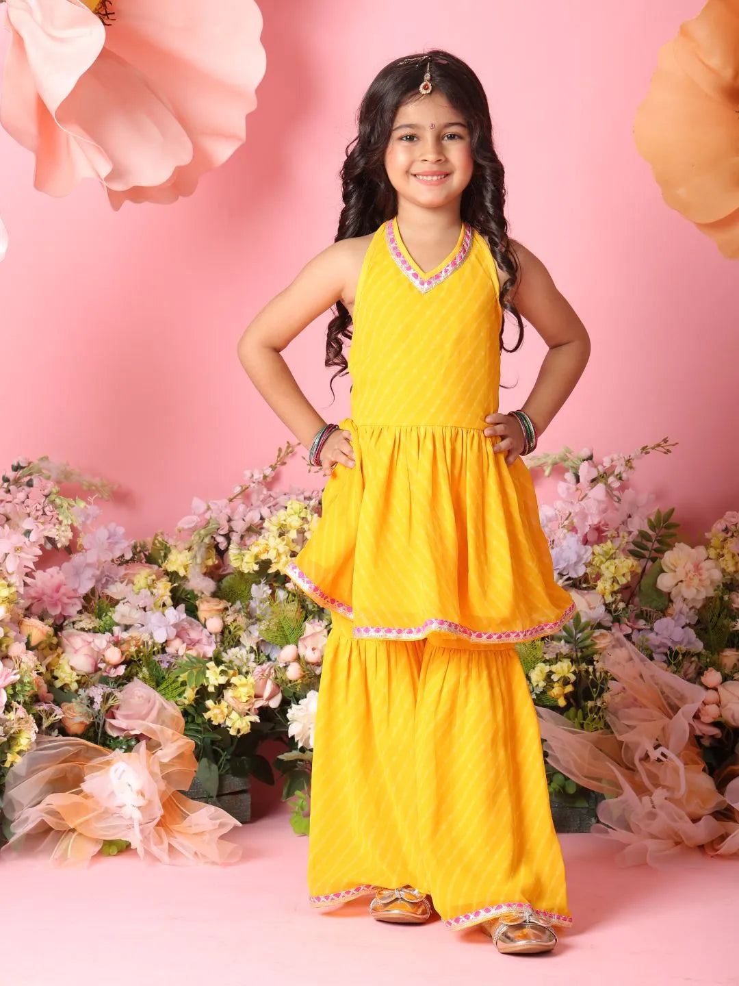 Young girl in a yellow traditional outfit with floral decorations on a pink background