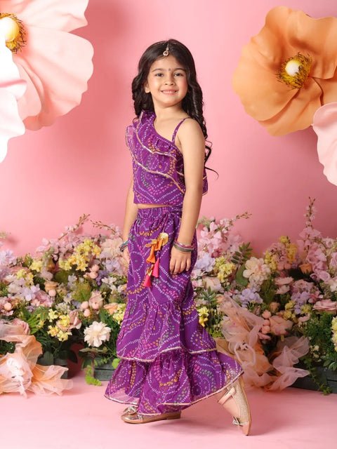 Young girl in a purple traditional outfit standing among flowers with a pink background