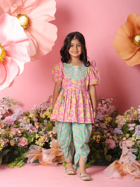 Young girl in a floral outfit standing in front of pink flowers and a pink background