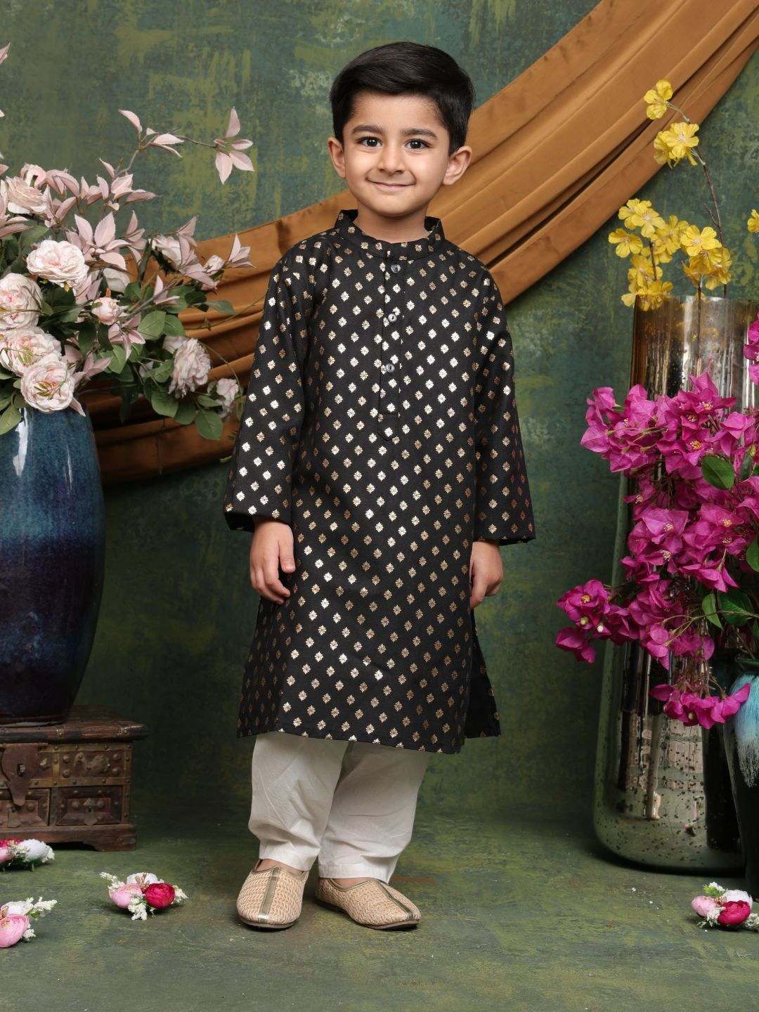 Child wearing a black kurta with white patterns in a decorative setting with flowers and a wooden frame.