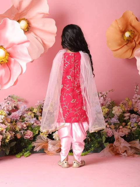 Child wearing a pink traditional outfit with a white dupatta against a pink floral background