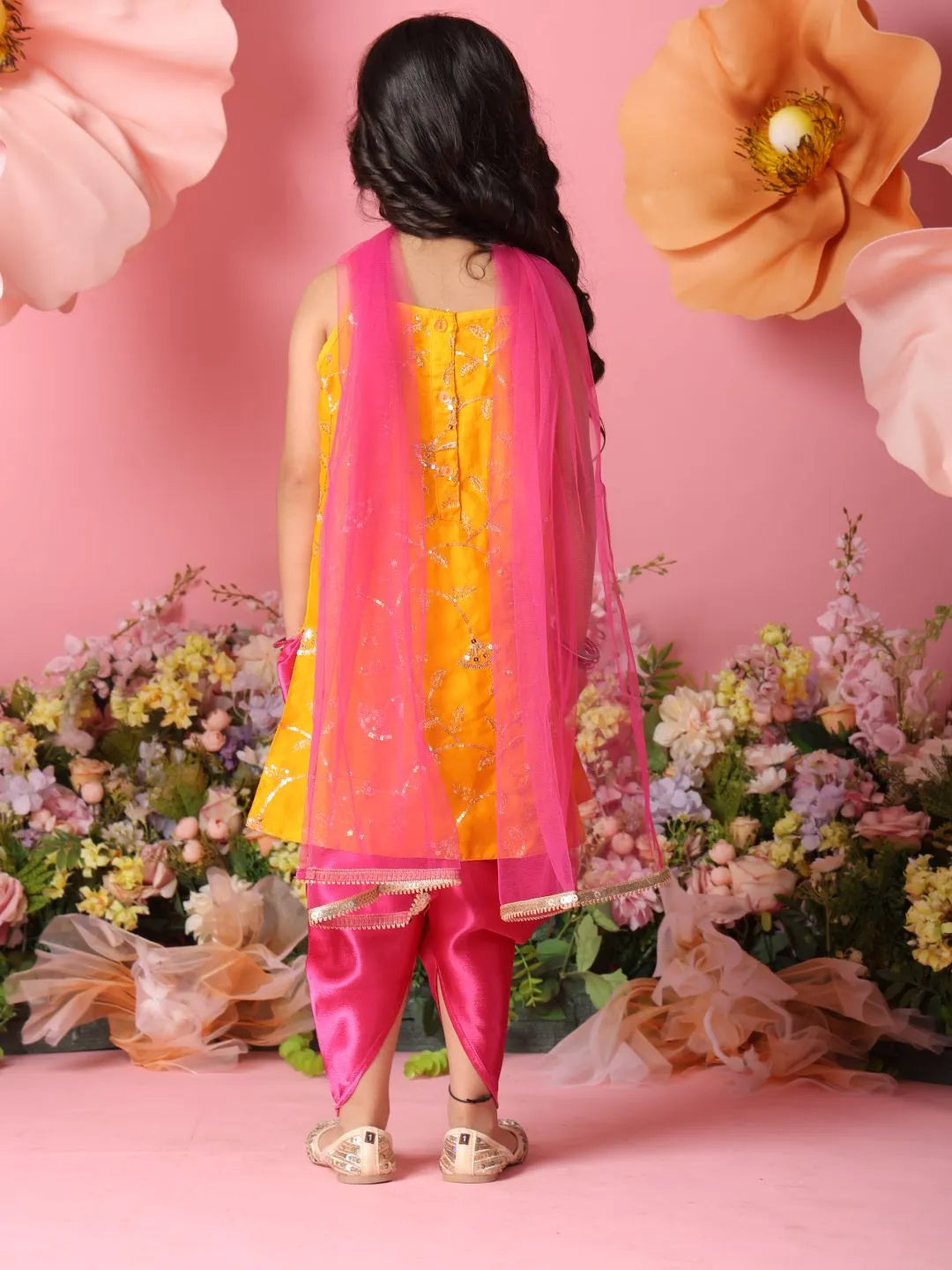 Child wearing a yellow and pink traditional outfit with floral decorations and pink background