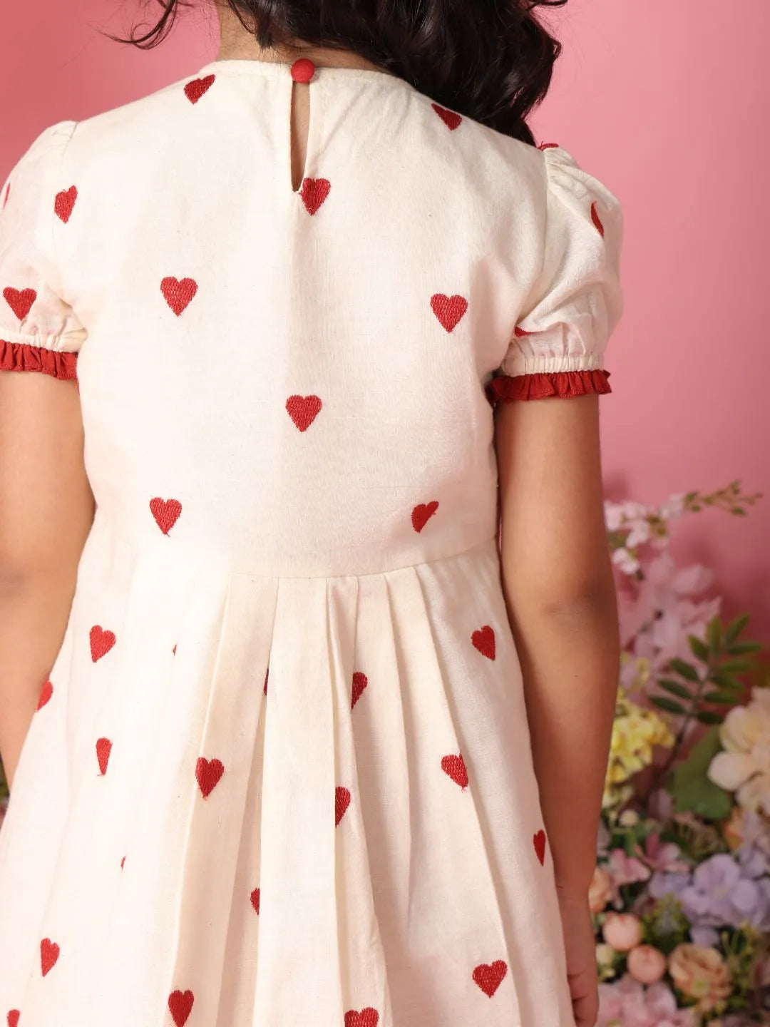 White dress with red heart patterns worn by a person against a floral background
