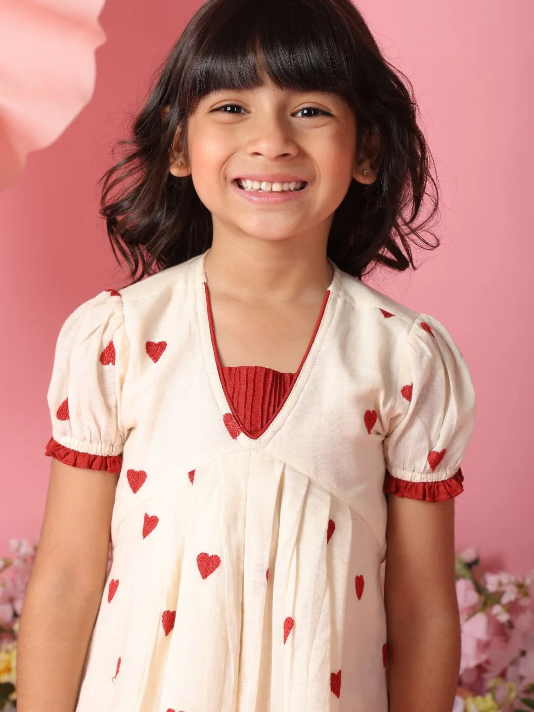 Young girl wearing a white dress with red heart patterns against a pink background
