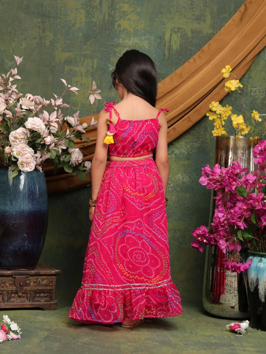 Woman in a pink traditional outfit standing in front of a decorative wall with flowers.