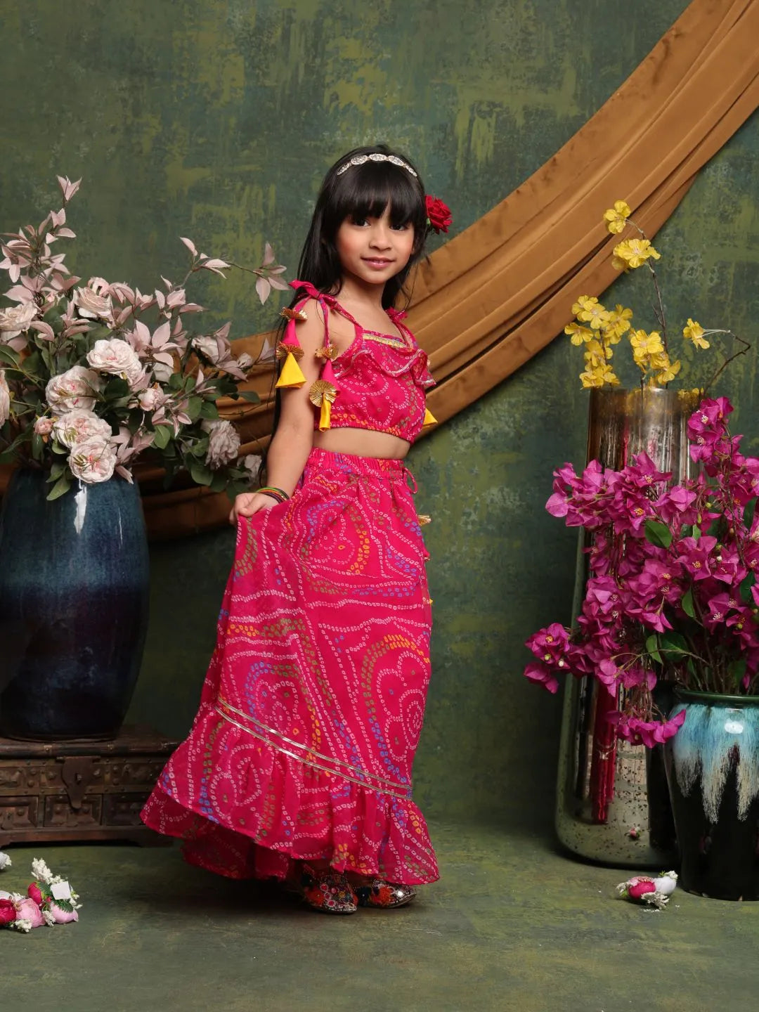 Young girl in a pink traditional outfit standing in front of floral decorations.