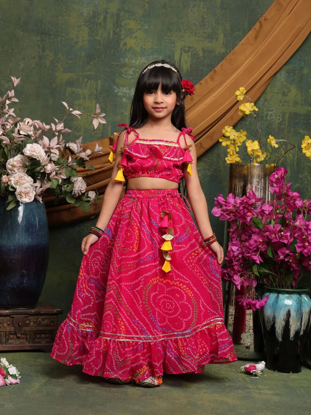 Young girl in a pink traditional outfit standing in front of floral decorations.