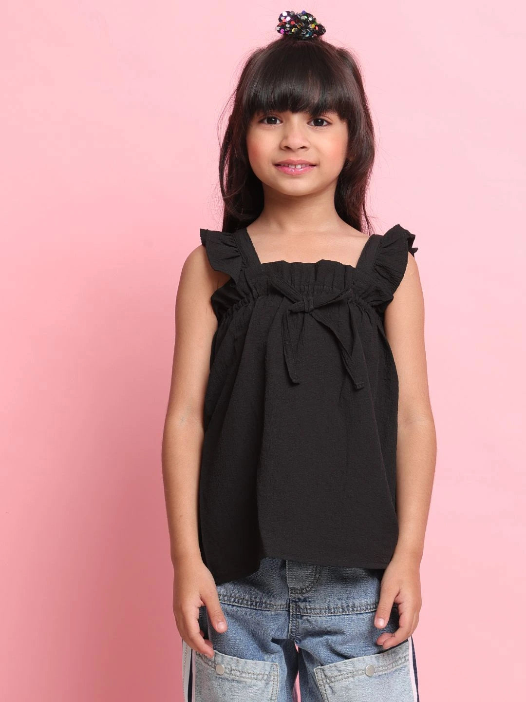 Young girl wearing a black top with ruffled straps against a pink background