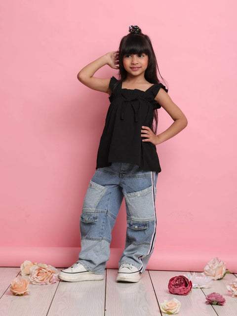 Young girl in black top and blue jeans posing against a pink background