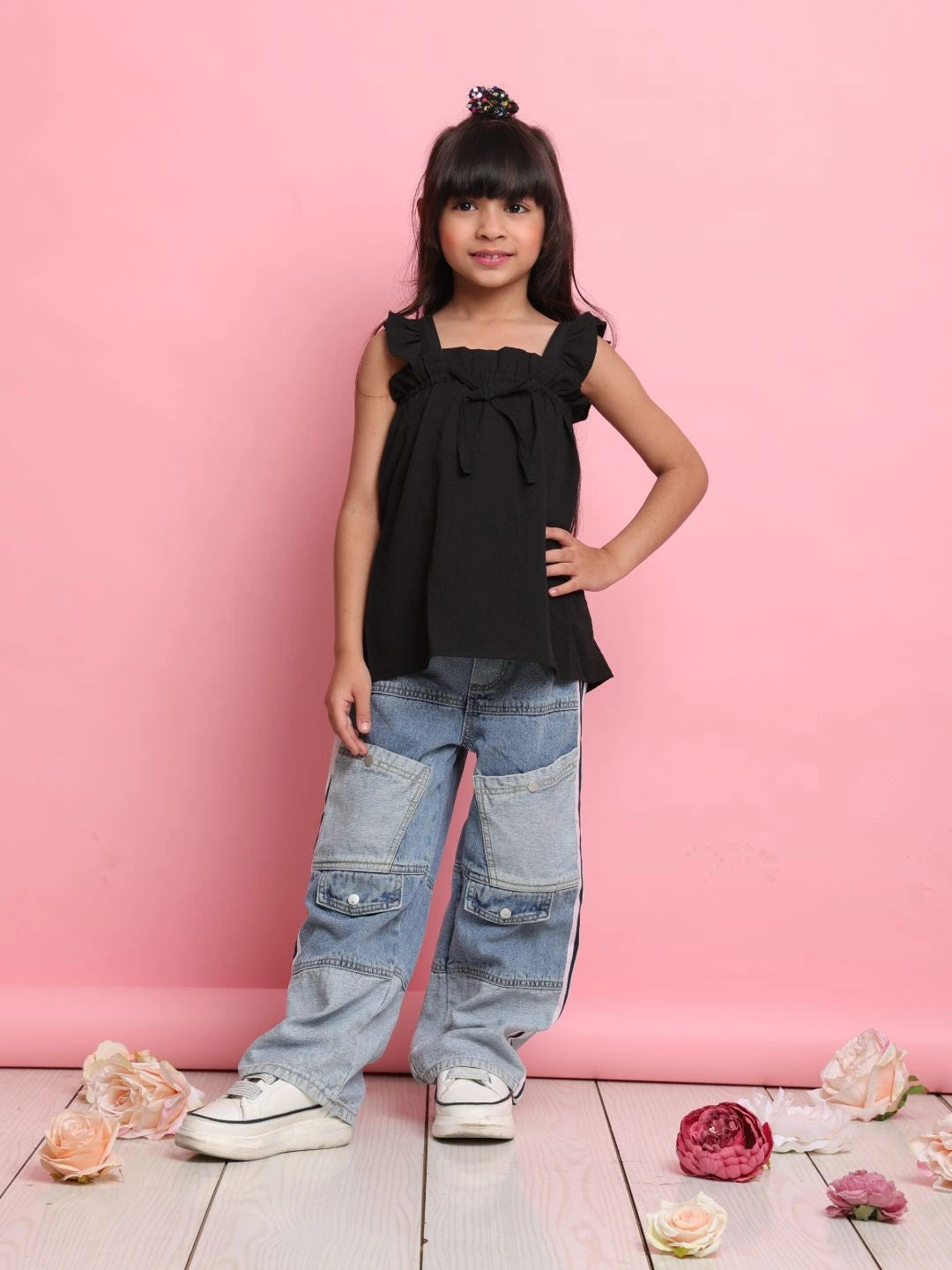 Young girl wearing a black top and blue jeans standing against a pink background