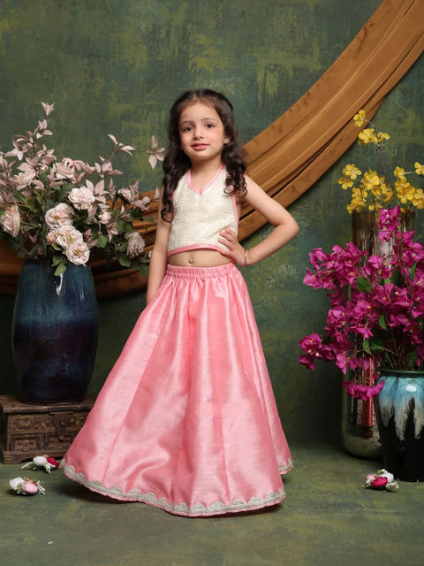 Young girl in a pink traditional outfit standing in front of floral decorations.