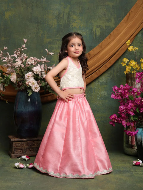 Young girl in a pink traditional outfit standing in front of floral decorations.