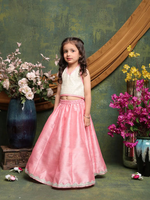 Young girl in a white top and pink skirt standing in front of floral decorations.