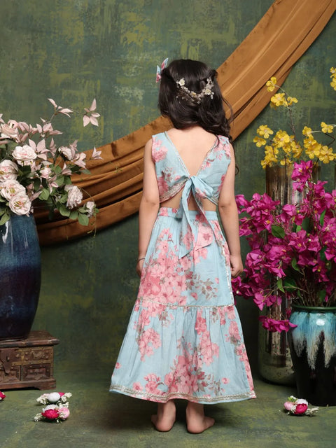 Woman in a floral dress standing in front of a decorative wall with flowers and vases.