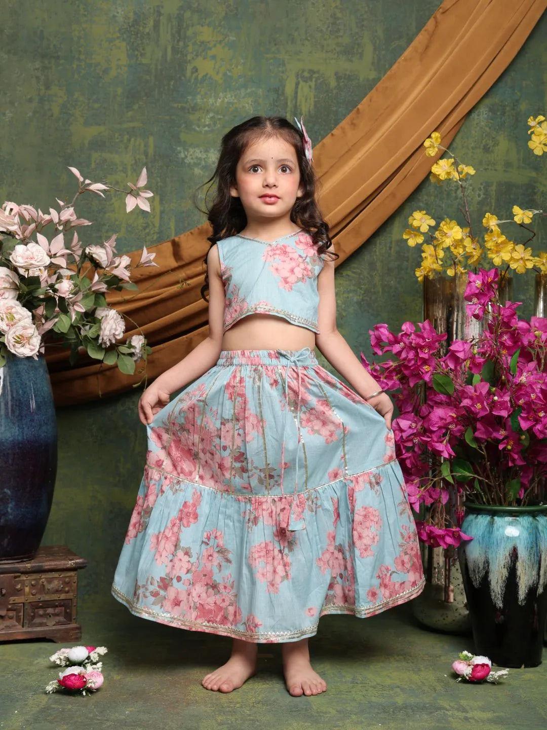 Young girl in a floral dress standing in front of a decorative wall with flowers.