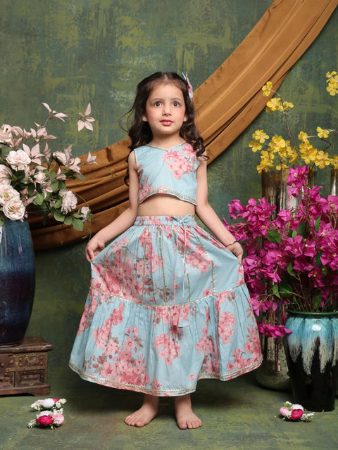 Young girl in a floral dress standing in front of a decorative wall with flowers.