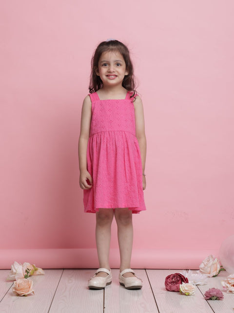 Young girl in a pink dress standing against a pink background with flowers on the floor.