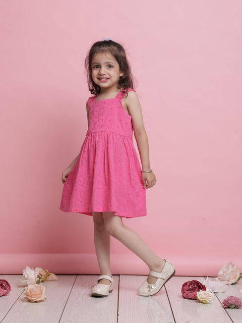Young girl in a pink dress standing against a pink background with flowers on the floor.