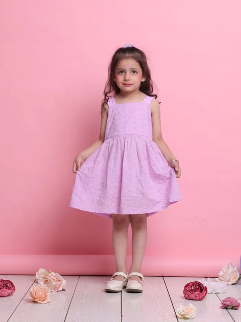 Young girl in a pink dress standing against a pink background with flowers on the floor.