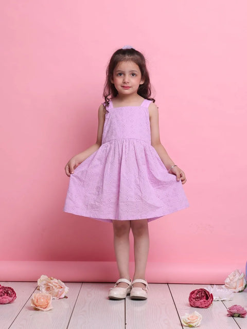 Young girl in a pink dress standing against a pink background with flowers on the floor.