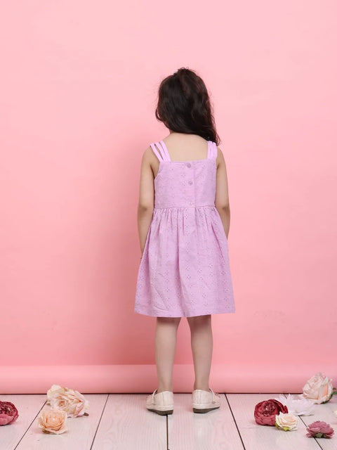 Child wearing a pink dress standing against a pink background with flowers on the floor.