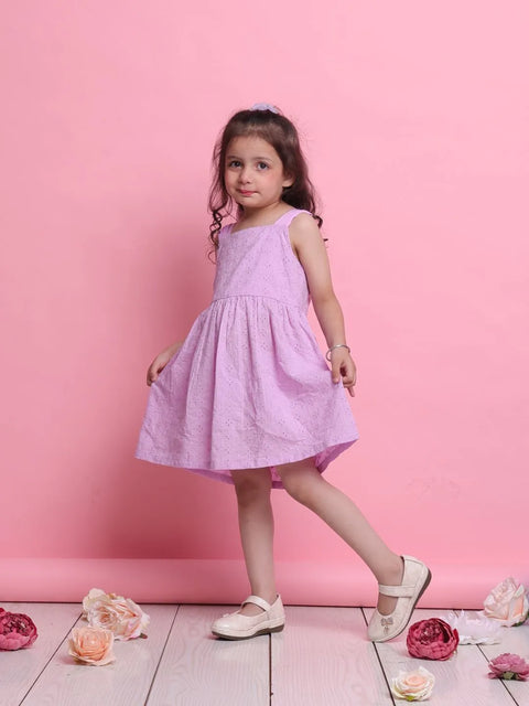 Young girl in a pink dress standing against a pink background with flowers on the floor.