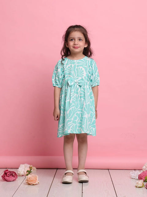 Young girl wearing a teal dress with white floral pattern against a pink background