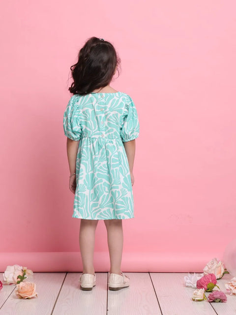 Child wearing a green dress with white patterns against a pink background