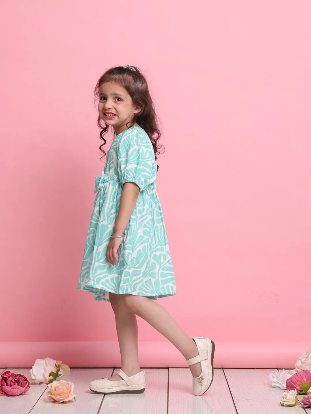 Young girl in a light blue dress standing against a pink background