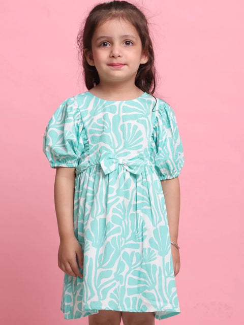 Young girl wearing a turquoise dress with white patterns against a pink background