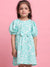 Young girl wearing a turquoise dress with white patterns against a pink background