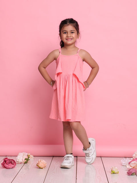 Young girl in a pink dress standing against a pink background with flowers on the floor.