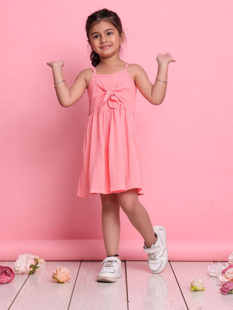 Young girl in a pink dress standing against a pink background with flowers on the floor.