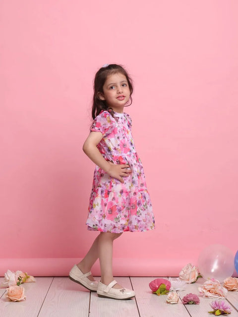 Young girl in a floral dress standing against a pink background with flowers on the floor.