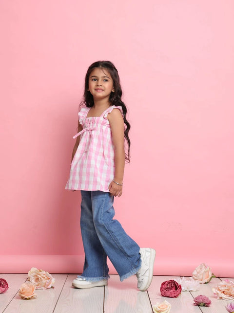 Young girl in a pink checkered top and blue jeans standing against a pink background
