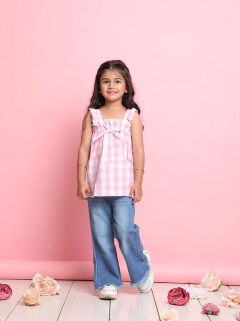 Young girl wearing a pink top and blue jeans standing against a pink background with flowers on the floor.