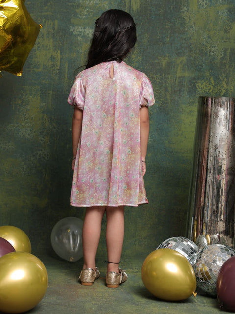 Child wearing a pink floral dress standing among colorful balloons against a textured green wall.