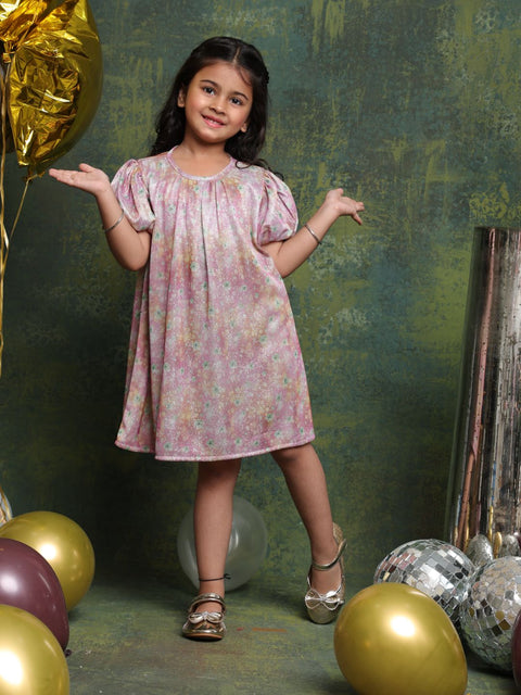 Young girl in a floral dress standing among balloons and disco balls against a textured green wall.