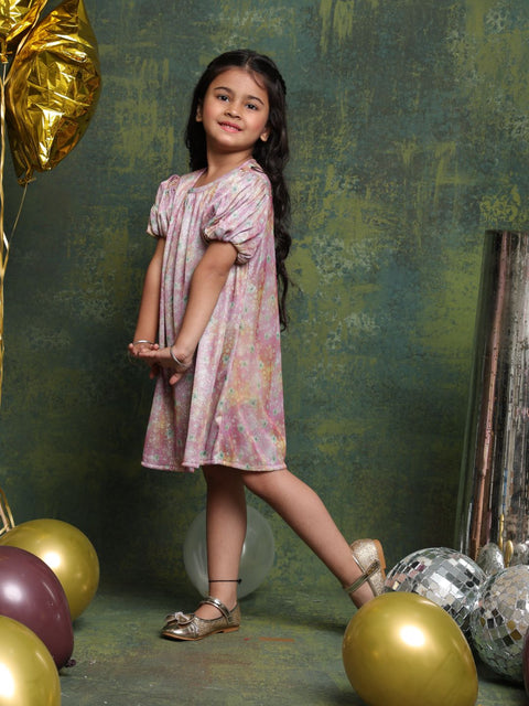 Young girl in a floral dress standing among balloons and decorative items against a textured green wall.