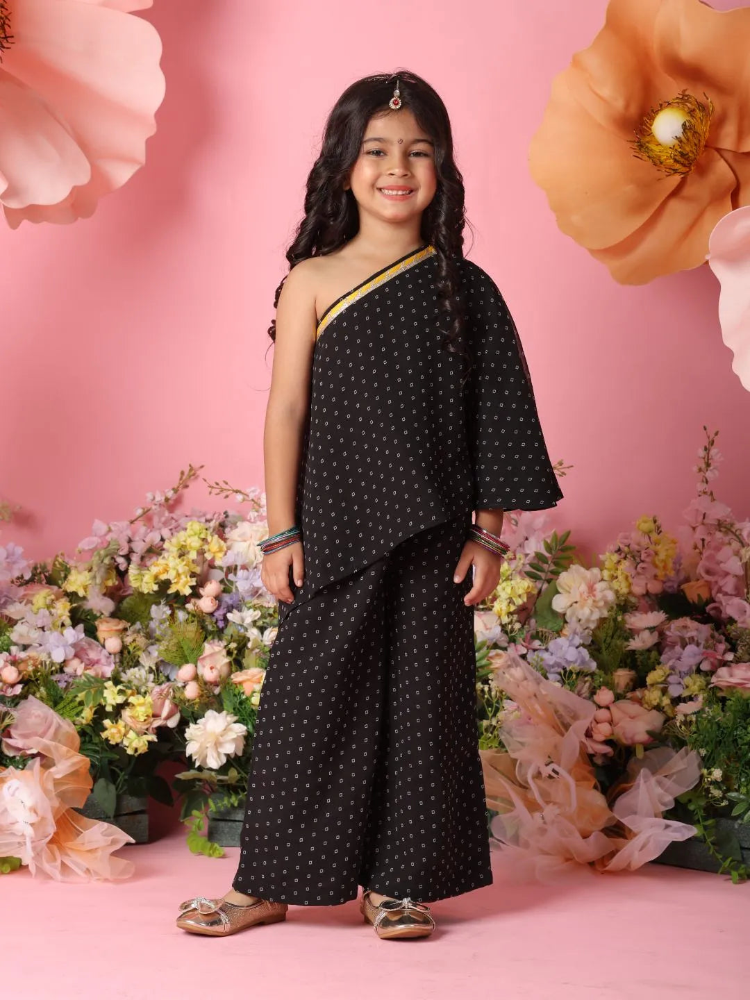 Young girl in a black polka dot outfit standing in front of pink flowers