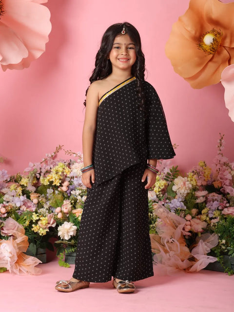 Young girl in a black polka dot outfit standing in front of pink flowers