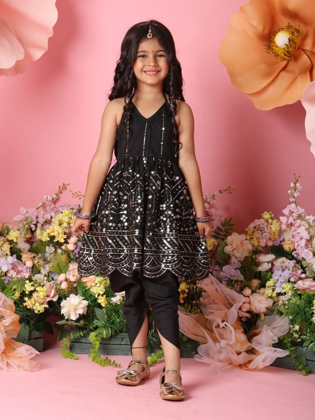 Young girl in a black sequined dress standing in front of pink flowers
